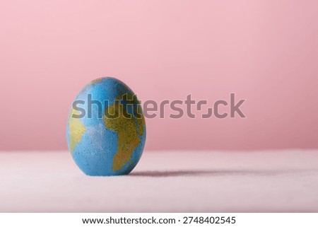Blue Easter egg with world map stands on pink background as symbol of global holiday, ecology and international unity theme.