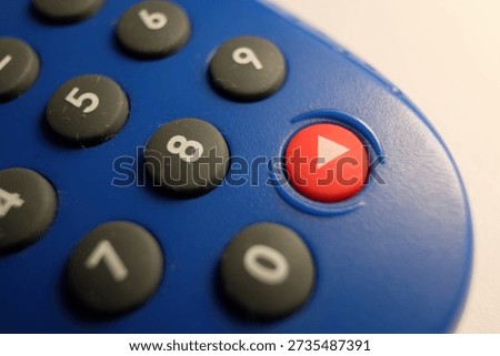 A blue electronic security token featuring a numeric keypad with black circular buttons and a prominent red "play" button. The plastic device has a textured grip and a shallow depth of field.