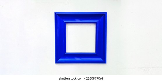 Blue Empty Picture Frame Isolated On White Wall With Copy Space. Object On Concrete Wallpaper For Decoration For Filling Text Or Adding Wording.