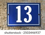 A blue enamel house number plaque, showing the white coloured number 13 (number thirteen). 