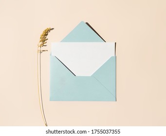Blue envelope with empty white paper letter and dry herb on beige background in boho style. Flat lay, top view. Summer, autumn concept. Greeting card mockup