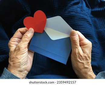 A blue envelope and a red heart in the hands of an elderly woman. Holiday greetings - Shutterstock ID 2359492157