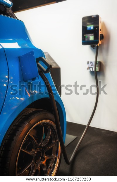 Blue EV / electronic vehicle parked and plunged in\
charged station. 