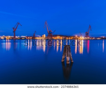 Blue evening sky over illuminated Gothenburg harbor with cranes and machinery.