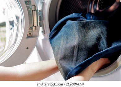 jeans de tela azul cargando en la lavadora a mano para limpiarlos.