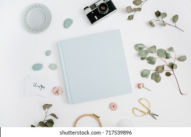 Blue family or wedding photo album  with blank space for text, eucalyptus leaf, retro camera and dry rose buds on white background. Flat lay, top view. Stock Photo