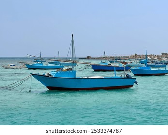 Blue fishing boats float serenely on the turquoise waters creating a peaceful scene by the coast. The calm sea and clear sky in the background complement the boats offering a tranquil marine landscape - Powered by Shutterstock