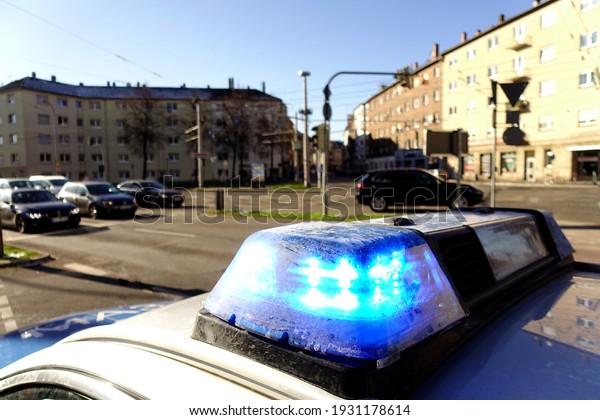 Blue flashing lights on a\
police car in a town in Germany. Houses, cars and streets in the\
background.