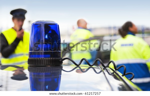 Blue flashlight on top of an unmarked police\
car, with a team of emergency medical service personnel in the\
background
