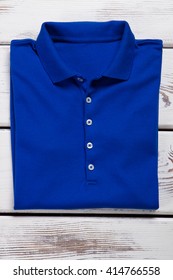 Blue folded t-shirt with collar. Polo t-shirt on wooden background. Woman's plain casual garment. Inexpensive clothing in stock.