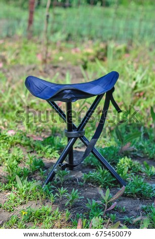 A blue folding high chair for camping on a summer green glade