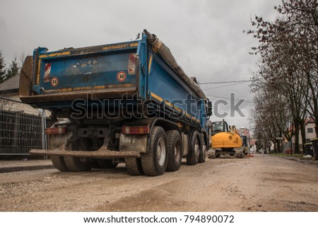 Blue four 4 axle dump truck is waiting for its next duty on a construction site on a town road. View of the back of the truck.