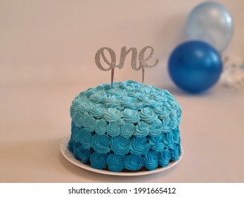 blue frosted first birthday cake with a one cake topper 
