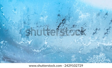 Blue frozen window background. Hoar frost on glass. Wallpaper with icy texture on windshield. Snowy windscreen from inside automobile. Film grain texture. Soft focus. Blur