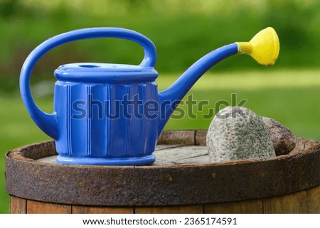 Blue garden watering can on an old barrel. Shallow depth of field