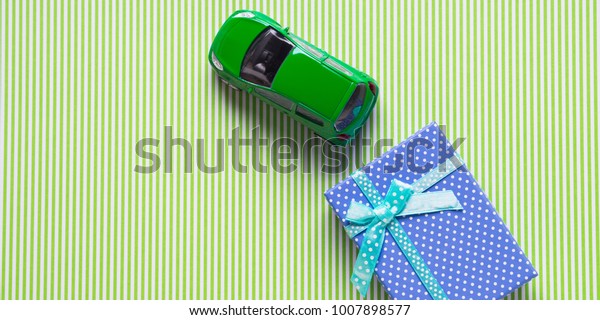 Blue gift box and a toy car on\
green background. Travel related present or car purchase\
concept