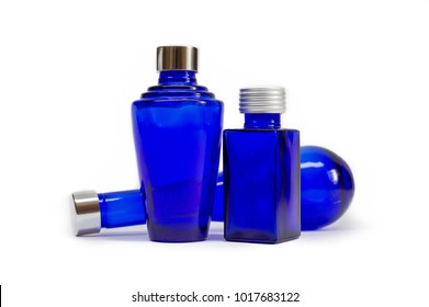 Blue Glass Bottles On White Background. Three Empty Decorative Cobalt Blue Bottles With Silver Lids, Each A Different Design. Glassware Intended For Cosmetics, Oils, Perfumes, Lotions And Potions.