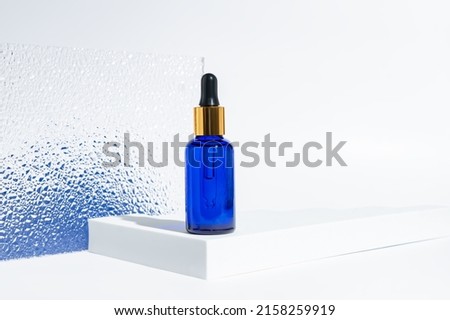 blue glass cosmetic bottle with a dropper on a white background with blue gradient. Natural cosmetics concept, natural essential oil and skin care products.