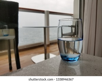 Blue glass of water focused in foreground with cruise ship balcony and ocean out of focus in background  - Shutterstock ID 1338946367