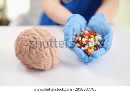 Blue gloved hands present assorted colorful capsules next to detailed brain model on bright table, creating clear medical concept for neuroscience, pharmacology, treatment planning, brain health