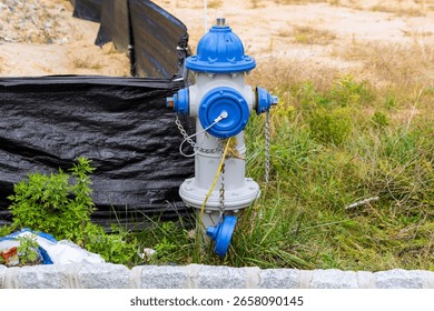 Blue, gray hydrant stands in construction zone, surrounded by grass debris, ready for emergencies.