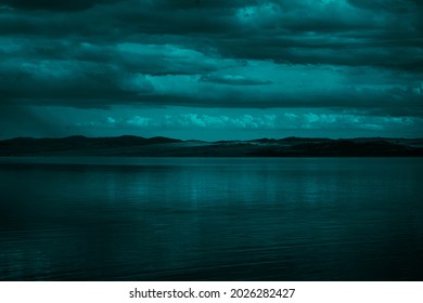   Blue green clouds over the sea. Toned seascape. Dark teal water and sky background with copy space for design.Rocky coastline on the horizon. Creepy, scary atmosphere, mood.                         