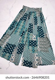 Blue green geometric print patchwork palazzo pants flat lay at gray marble background. Boho style wide leg cotton rayon yoga women's trousers. Clothes, apparel, fashion, vacation collection, shopping