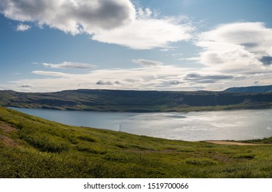 Blue and green misty mountains surrounding still bay, overlooking small farmland, Westjords Iceland