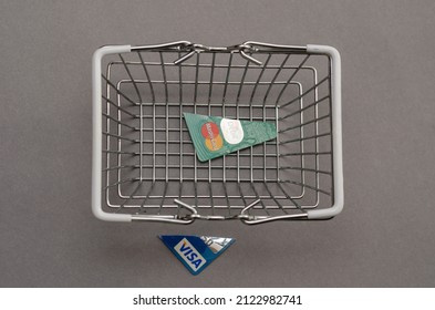 Blue and green pieces of credit cards and an empty shopping cart. Cut off pieces of Visa and MasterCard bank cards against a gray background. Selective focus. Kiev, Ukraine - 01 05 2022.