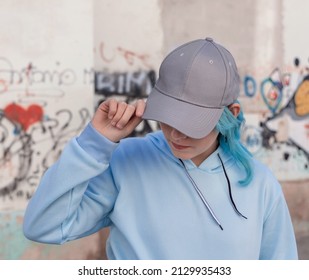 Blue haired Teenage girl in blue hoodie and baseball cap touching her cap. Blue haired teen girl stays outdoors against graffiti wall. Clothing and cap mockup  - Powered by Shutterstock