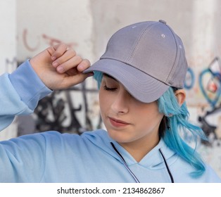 Blue Haired Teenage Girl In Blue Hoodie And Baseball Cap With Closed Eyes Touching Her Cap. Blue Haired Teen Girl Stays Outdoors Against Graffiti Wall. Cap Mockup 