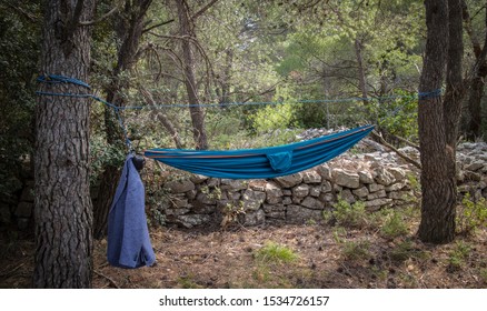 Blue hammock between two trees in the forest, with a jacket hanging on one side 