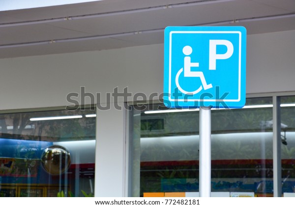 blue handicapped sign mark parking spot, disabled\
parking permit sign on pole with convenience store in gas station\
area background, copy\
space