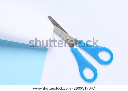 Blue handled craft scissors with serrated blades and ruler markings on a white and light blue background, the scissors are open, ready for cutting paper or other materials