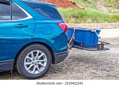 Blue Hatchback Car Parked On Gravel With Hitch Cargo Carrier Holding Tied Down Rubber Storage Box On Back - Closeup And Cropped