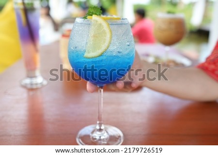 Blue Hawaii Italian soda decorated with  Lemon in glass. woman's right hand picked blue drink glass in beverage shop. Sweet drink there is soda to refresh the body while thirsty or hot in summer.