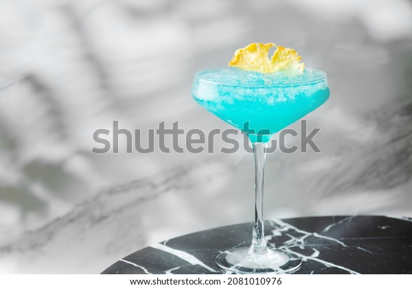 Blue Hawaiian Cocktail in\
glass summer drink concept. blue cocktail with pineapple on marble\
table.
