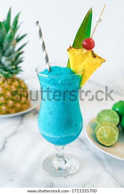 Blue Hawaiian Tropical Cocktail Drink Slush Mixed\
Blended with Pineapple Cherry and Lime on Marble Countertop Drink\
with Straw