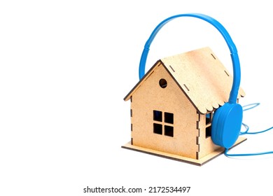 Blue headphones put on a miniature wooden house model isolated on white background. House noise and acoustic insulation concept.