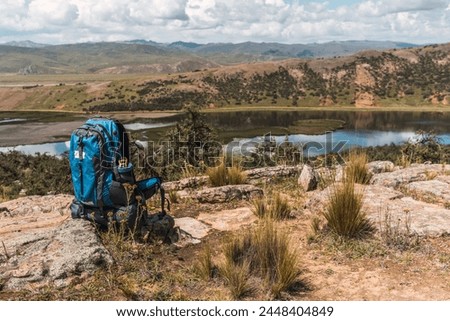 blue hiking backpack placed on the rocks in the mountain surrounded by green vegetation and natural sunlight and with storm clouds with a lake in the background of the Andes mountain range