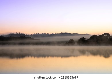 blue hour at a lake with forest in the backgroudn and fog lots of colors in the sky and reflection in the water