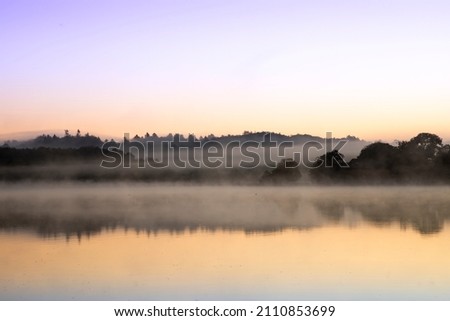 blue hour at a lake with forest in the backgroudn and fog lots of colors in the sky and reflection in the water