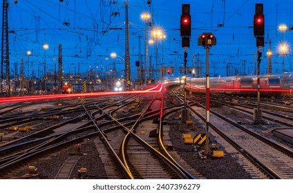 Blue hour at the main station of Frankfurt Main Germany with railway infrastructure technology, signals, crossings, catenary, glistening tracks, switches at twilight. Blurred train lights in motion.  - Powered by Shutterstock