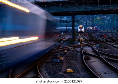 Blue hour at main station of Hagen Westphalia Germany with many lights, signals, catenary, glistening tracks, switches and trains in motion. Railway infrastructure and technology at morning twilight. 