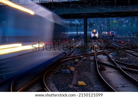 Blue hour at main station of Hagen Westphalia Germany with many lights, signals, catenary, glistening tracks, switches and trains in motion. Railway infrastructure and technology at morning twilight. 