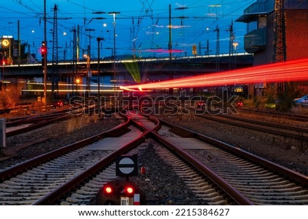 Blue hour at the main station of Hagen Westphalia Germany with railway infrastructure technology, signals, crossings, catenary, glistening tracks, switches at twilight. Train lights in motion. 