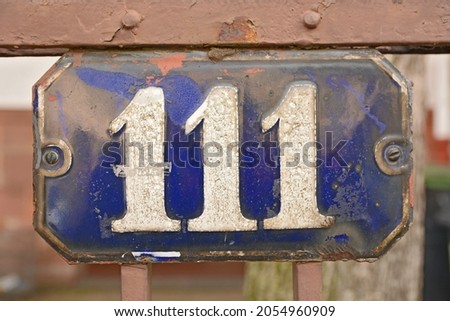 A blue house number plaque, showing the number hundred and eleven (111) 