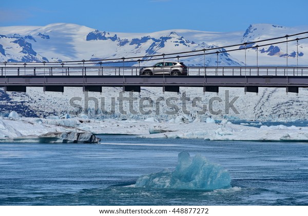 Blue iceberg floating below a passing car at\
Jokulsarlon Glacier Lagoon, which is formed from melting glacier\
due to global warming