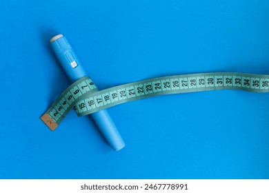 Blue injector dosing pen for subcutaneous injection of antidiabetic medication, anti-obesity medication on a blue background. Measuring tape around the injector.  Drug and weight loss - Powered by Shutterstock