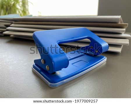Blue iron metal office punch for punching holes in sheets of paper and documents on the working business table in the office. Stationery.